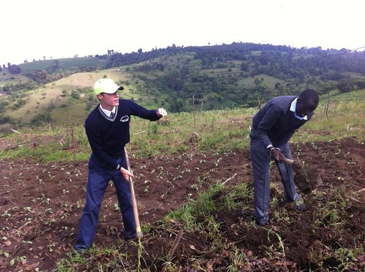 Stephen Valvano and Edwin Rutto till the ground. They are wearing their school uniforms.